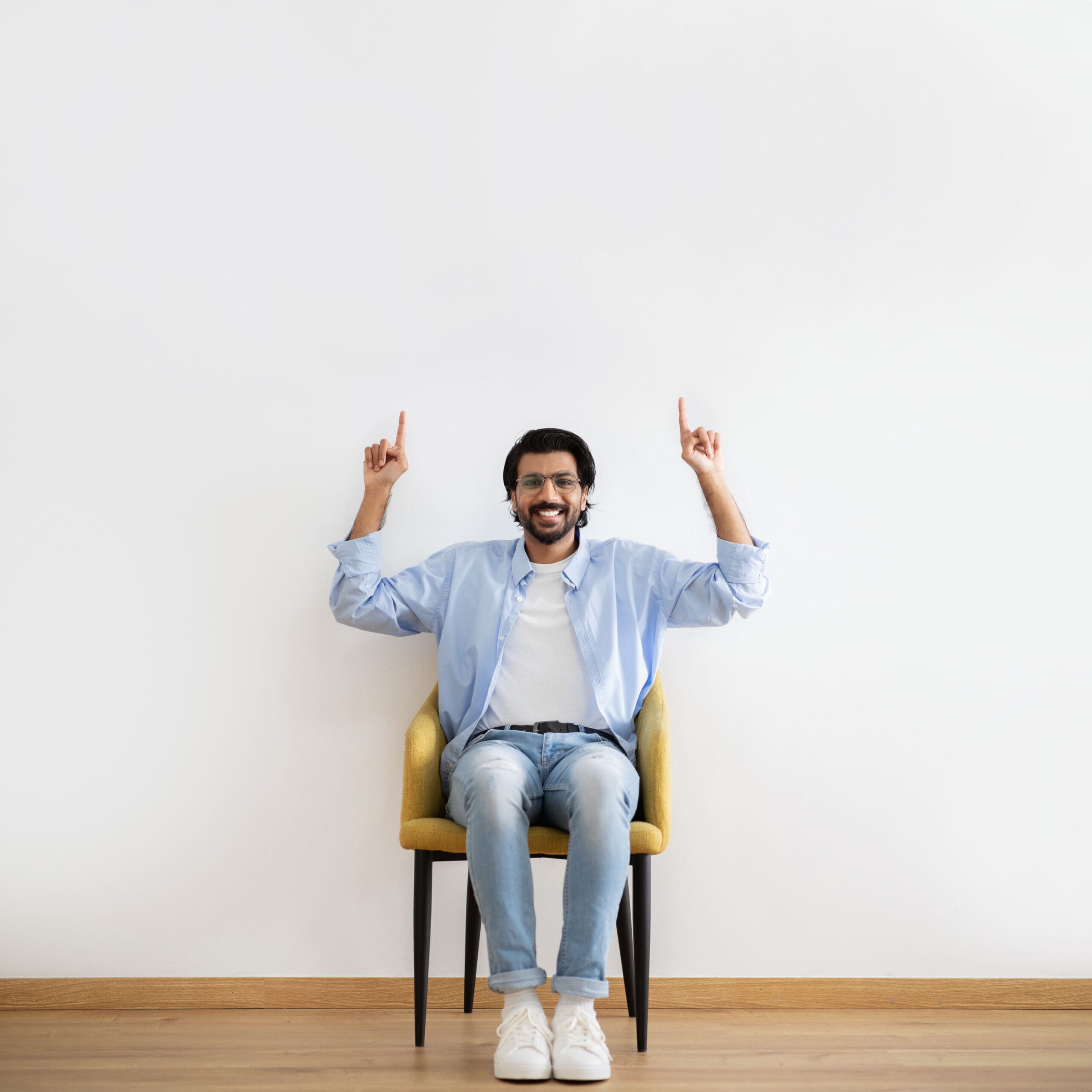 A joyful Muslim man sitting in a chair, raising his fingers up in a gesture of happiness and triumph which displays the successful setup of his Virtual Private Server hosting, symbolizing his satisfaction with the service